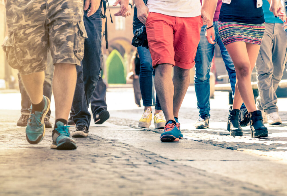Crowd of people walking on the street - Detail of legs and shoes moving on sidewalk in city center - Travellers with multicolor clothes on vintage filter - Shallow depth of field with sunflare halo